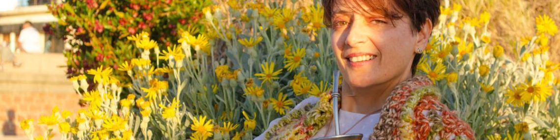 A woman smiles while drinking traditional mate among yellow flowers in Montevideo.
